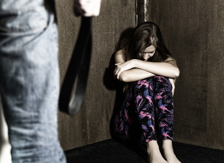 frightened woman sitting in the corner with a faceless man holding a belt, a conceptual shoot...