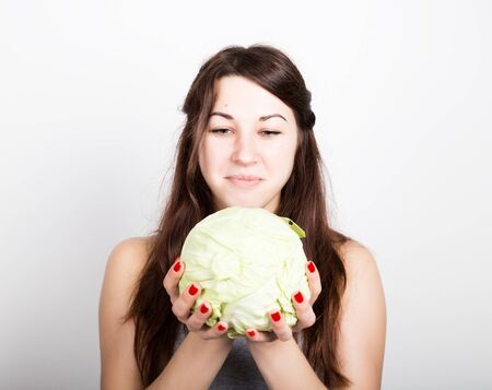 beautiful young woman eating an vegetables. holding cabbage, she stares at the head of cabbage....