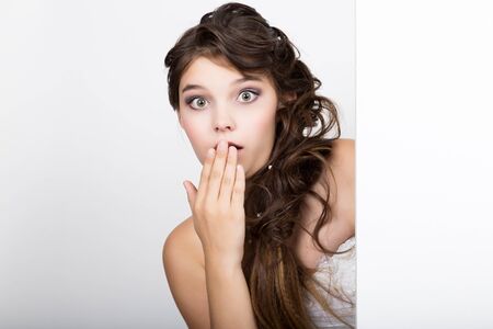 Smiling happy young woman standing behind and leaning on a white blank billboard or placard, expresses different.の写真素材