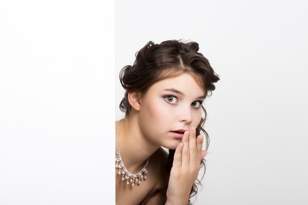 Smiling happy young woman standing behind and leaning on a white blank billboard or placard, expresses different.の写真素材