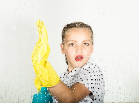 Smiling little housewife washed the window with a cloth and detergent. Large window glass in foam. Housework conceptの写真素材