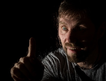 Drops of water on a glass, hand and male face. adult man standing at the window on a rainy day