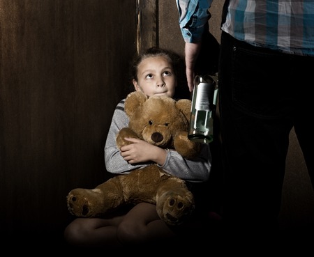 Sad little girl sitting against the wall in despair. In his hands he holds an teddy bear. drunken man threatensの写真素材