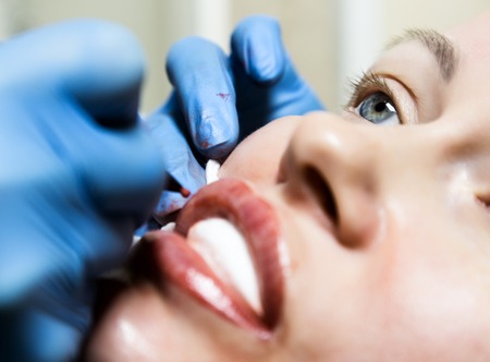 Cosmetologist applying permanent make-up. Young beautiful woman having cosmetic tattoo on her lips....