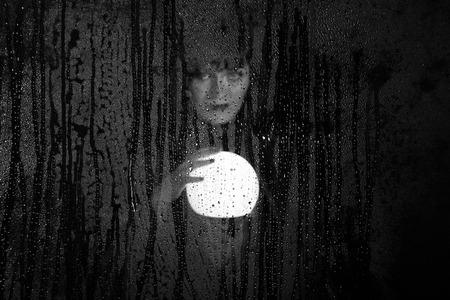 Smooth portrait of female model, posing behind transparent glass covered by water drops. woman...