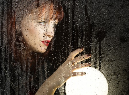 Smooth portrait of female model, posing behind transparent glass covered by water drops. woman...