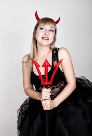 beautiful young woman is wearing a sexy devil costume with a trident.