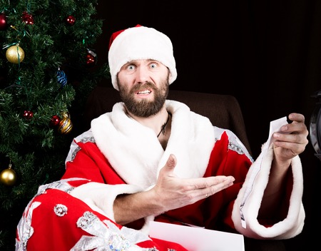 bad brutal Santa Claus discontentedly reads letter with the wishes, on the background of Christmas...