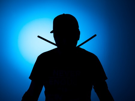 silhouette Expressive young drummer with drum stick on a blue background.の写真素材