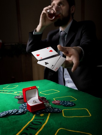 man in a business suit drinking brandy and throws cards with losing combination. casino chips, precious ring on green poker table. gambling addiction.の写真素材