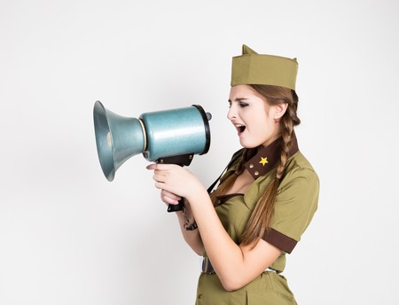 sexy fashionable woman in military uniform and garrison cap, holding bullhorn and screaming