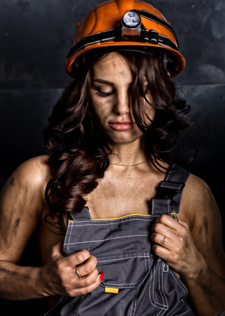 close-up portrait sexy female miner worker in coveralls over his naked body, helmet on the head with a flashlightの写真素材