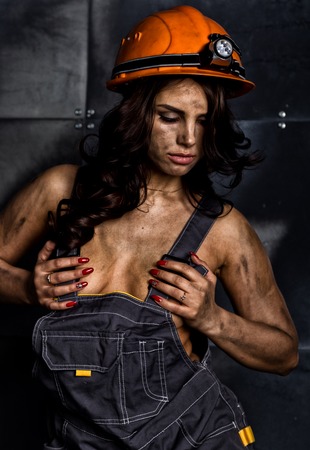 close-up portrait sexy female miner worker in coveralls over his naked body, helmet on the head with...