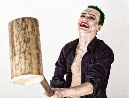 guy with crazy joker face, green hair and idiotic smile. carnaval costume. holding hammer for cricketの写真素材