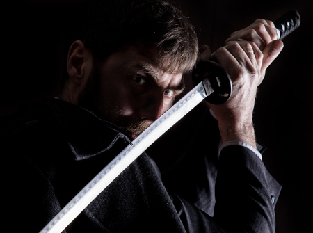 stern angry businessman in a wool coat with sword in dark background