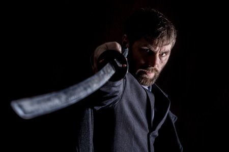 stern angry businessman in a wool coat with sword in dark backgroundの写真素材