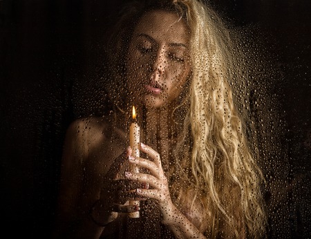 curly nude blonde woman with candle on dark backgroundの写真素材