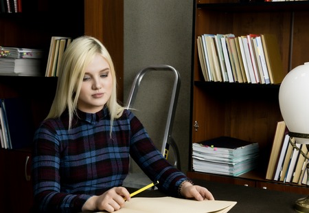 young woman reading a big book in library. bookshelves with booksの写真素材