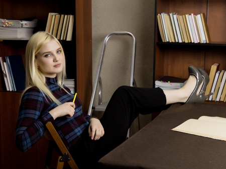 young female librarian reading a big book in library. bookshelves with books, stepladder and desk with lampの写真素材
