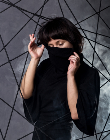 beautiful fashionable lady wearing a gothic black dress with high collar, poses in white smoke on a grey background.の写真素材