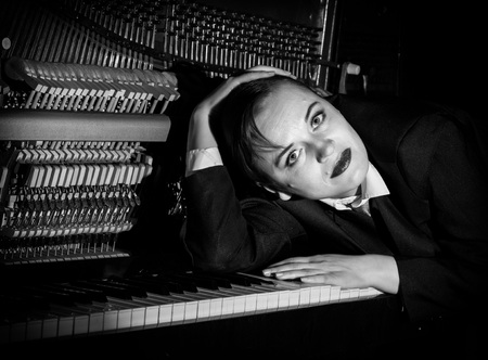 female musician dressed in a mans suit lies on a piano keyboard
