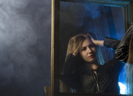 beautiful young woman in a leather jacket posing on a mirror backgroundの写真素材