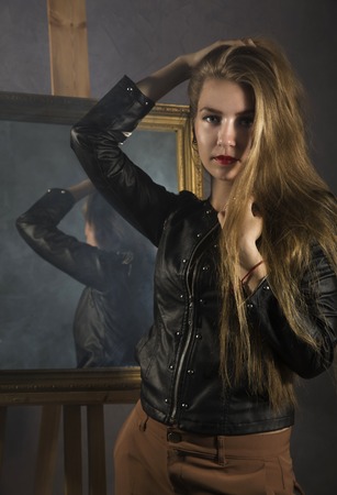 beautiful young woman in a leather jacket posing on a mirror backgroundの写真素材