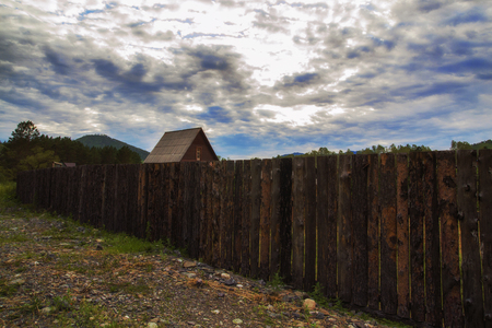 small house by the old wooden fence in the village on a dark cloud background.の写真素材