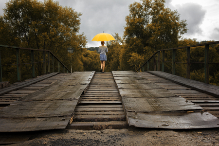 Beautiful woman hold yellow umbrella and walking on a old bridge in the countryside under rainの写真素材
