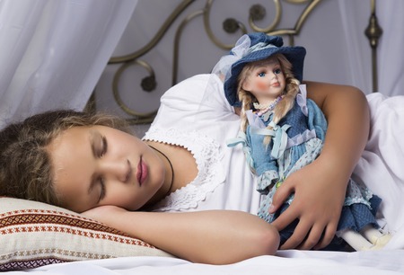 beautiful little girl sleep in a bed and hug her baby doll.の写真素材