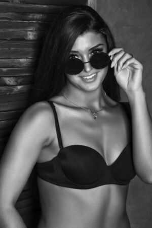 sexy woman wearing in black bra and sunglasses posing on a gray background. black and whiteの写真素材