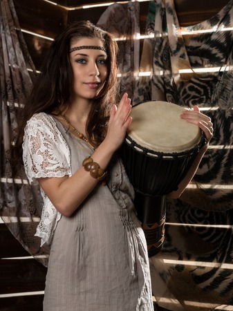 Young hippie boho woman having fun ans plays the Jamaica drum. Hippie style on a wooden backgroundの写真素材