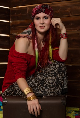 Cheerful hippie boho redhead woman poses with old suitcase on a wooden wall background.の写真素材