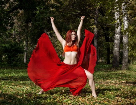 beautiful woman in red dress dancing in a autumn forestの写真素材