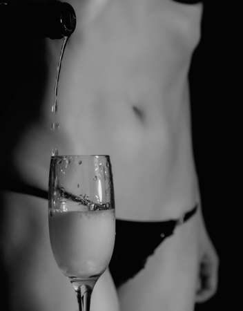 sexy body woman in black underwear pours champagne in glass.の写真素材
