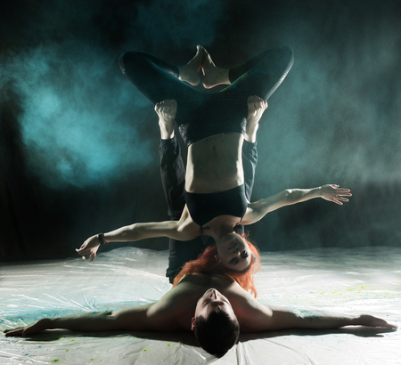 sports man and woman doing acroyoga exercises in a dark room with colorful smokeの写真素材