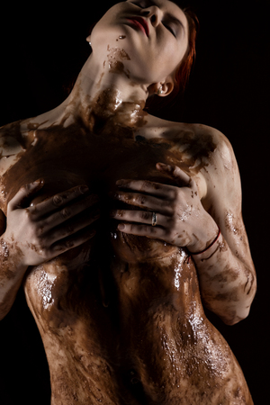 sexy nude woman covered sweet cream chocolate on a dark backgroundの写真素材