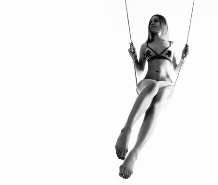 Perfect slim girl with a rope posing on a light background. Woman with sexy athletic body on a swing. free space for your text. black and whiteの写真素材