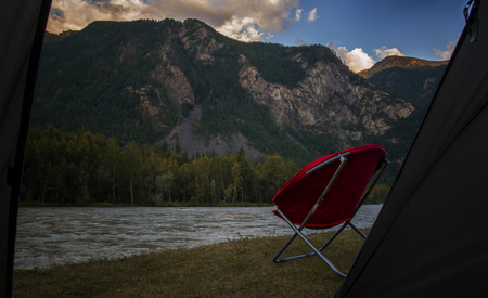red armchair on the bank of mountain river. Cloud over the mountain range. Blue sky and green grassの写真素材