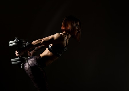 Young athletic woman in sportswear with a dumbbellson a dark background. free space for textの写真素材