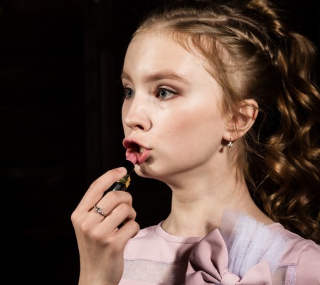 small beauty painting her lips of pink lipstick on a dark backgroundの写真素材