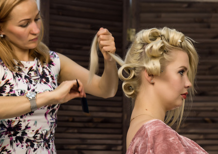 Hairdresser does hairstyle for luxurious blond woman. coiffure in the form of big curl. Concept...