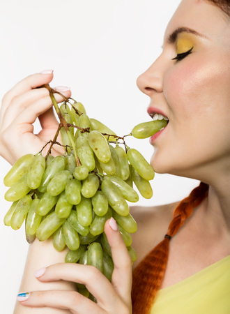 Beautiful redhead woman is eating grapes. concept of healthy eatingの写真素材