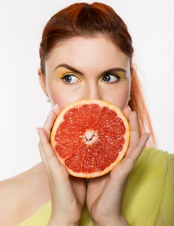 Young redhead woman with grapefruit in her hands studio portrait on a white background. concept of healthy eatingの写真素材