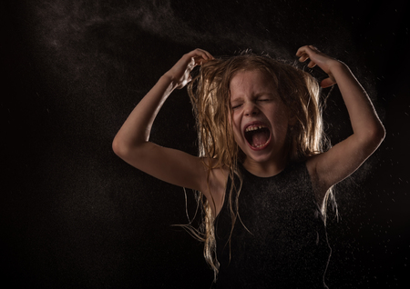 young girl with live emotions dancing under water drops. child screaming on a dark background with water splashの写真素材