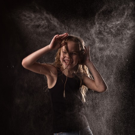young girl with live emotions dancing under water drops. child splashing water on a dark background