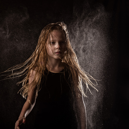 young girl with live emotions dancing under water drops. child splashing water on a dark backgroundの写真素材