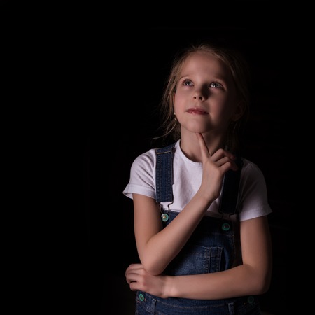 beautiful blonde little girl on a dark background. She stands in different poses and shows different emotions. free space for your textの写真素材