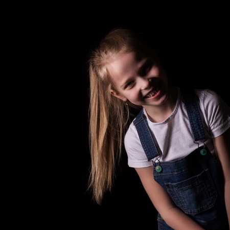 beautiful blonde little girl on a dark background. She stands in different poses and shows different emotions. free space for your textの写真素材
