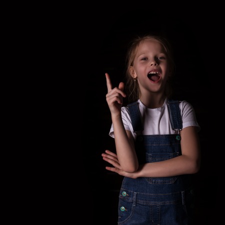 beautiful blonde little girl on a dark background. She stands in different poses and shows different emotions. free space for your textの写真素材